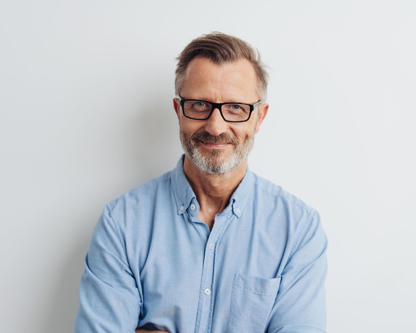 Bearded middle-aged man wearing glasses posing over a white studio background with copy space looking at the camera with a friendly smile