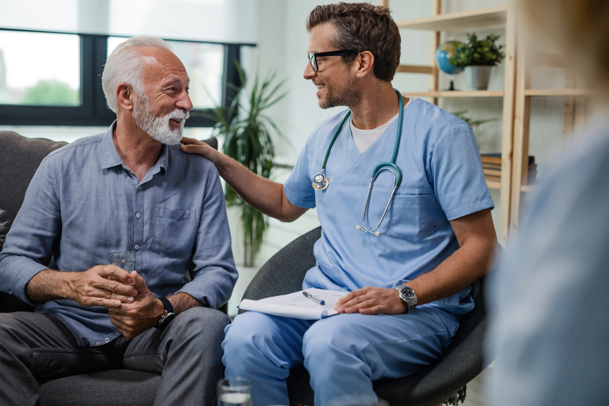 Happy doctor talking to senior male patient while being in a home visit.